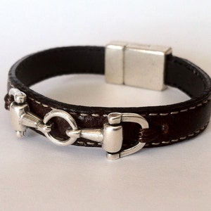 May include: A brown leather bracelet with a silver magnetic clasp and a silver horse bit design.