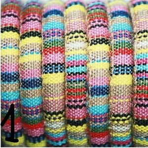 Puede incluir: Primer plano de un cord&oacute;n de tela a rayas de colores, tejido con varios colores, incluyendo amarillo, rosa, azul y negro. El cord&oacute;n est&aacute; tejido apretado y tiene una superficie texturizada.