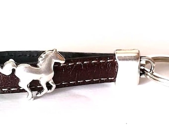 May include: A brown leather keyring with white stitching and a silver-coloured horse charm. The keyring has a silver metal clasp and key ring. The leather strap is approximately 13 cm long.