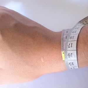 May include: A white measuring tape wrapped around a wrist, showing a measurement of 16 inches.
