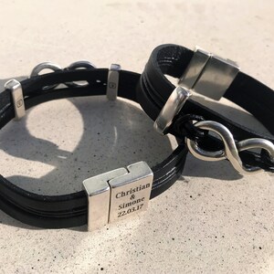 May include: Two black leather bracelets with silver infinity symbol charms. One bracelet has a silver clasp engraved with "Christian & Simone 22.03.17".