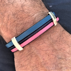 Puede incluir: Un brazalete de cuero negro, rosa y plateado con cierre de broche.