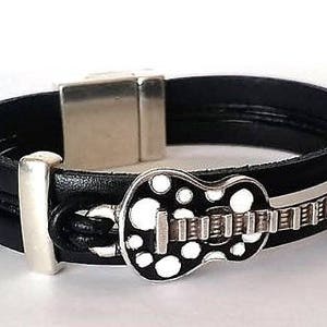 May include: Black leather bracelet with a silver magnetic clasp and a silver guitar charm with white polka dots.