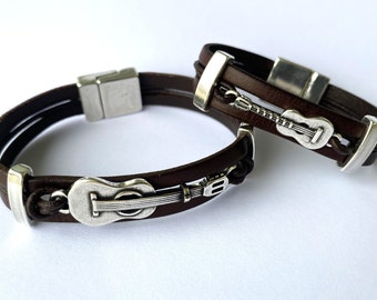 May include: Two brown leather bracelets with silver guitar charm accents. The bracelets have a magnetic clasp.