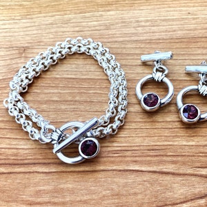 May include: A silver chain bracelet with a toggle clasp and a purple gemstone. Matching earrings with purple gemstones and silver hoops.