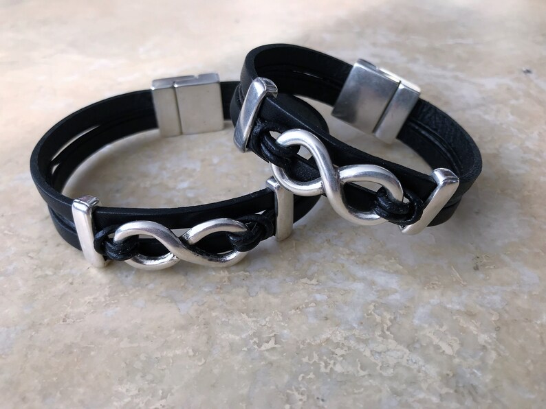May include: Two black leather bracelets with silver infinity symbol charms. The bracelets have magnetic clasps.