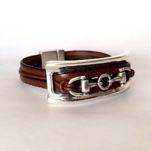 May include: A brown leather bracelet with a silver metal buckle and a silver metal horse bit design.