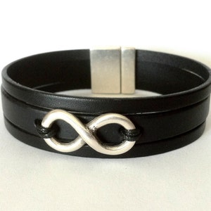 Peut inclure: Un bracelet en cuir noir avec un charme en argent en forme d'infini et un fermoir magnétique.