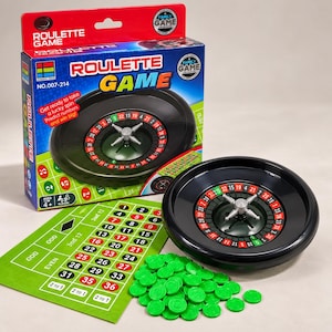 May include: A roulette game set featuring a black plastic roulette wheel with a silver center, a green betting mat with numbered grid and betting options, and a pile of green plastic chips. The packaging box displays the text Roulette Game.