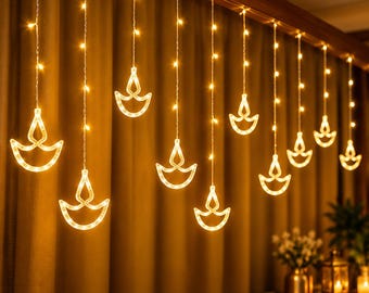 May include: A string of warm white LED curtain lights featuring hanging diya lamp silhouettes. The lights are arranged in vertical strands suspended from a horizontal wire, with each strand ending in a glowing, flame-shaped diya outline.
