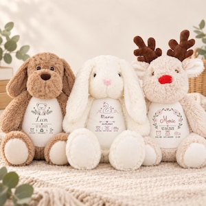 Op de afbeelding: Drie pluche knuffels: een bruine hond, een wit konijn en een beige rendier met bruin gewei en een rode neus. Elk speeltje heeft een wit buikvlak bedrukt met een naam, datum en geboortegegevens zoals een klok, weegschaal en liniaal.