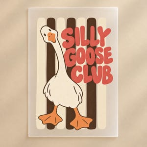 Op de afbeelding: Een rechthoekige wandkunstprint met een witte gans met oranje voeten en snavel. De achtergrond bestaat uit verticale crème en donkerbruine strepen. De tekst SILLY GOOSE CLUB staat in grote, dikke, rode, afgeronde hoofdletters.