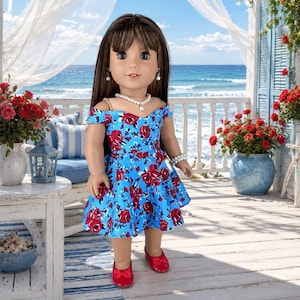 K&ouml;nnte beinhalten: Eine Puppe mit langem braunem Haar tr&auml;gt ein schulterfreies blaues Kleid mit rotem Rosenmuster, eine wei&szlig;e Perlenkette, Perlenohrringe, ein wei&szlig;es Perlenarmband und gl&auml;nzende rote flache Schuhe mit kleinen Schleifen an der Vorderseite.