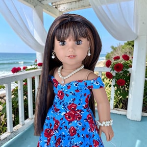 K&ouml;nnte beinhalten: Eine Puppe mit langem braunem Haar und Pony tr&auml;gt ein leuchtend blaues schulterfreies Kleid mit einem roten Rosenmuster. Die Puppe ist mit einer wei&szlig;en Perlenkette, einem passenden Perlenarmband und kleinen Perlenohrringen geschm&uuml;ckt.
