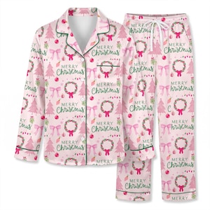 Può includere: Un set di pigiama rosa chiaro con un motivo ripetuto di alberi di Natale verdi, ghirlande rosse e verdi, fiocchi rosa e il testo Merry Christmas in corsivo verde. La camicia a maniche lunghe abbottonata ha un colletto e una tasca.