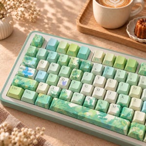 May include: A mechanical keyboard featuring a QWERTY layout with custom keycaps in shades of green, blue, and white. Several keys display printed butterfly and floral patterns, while the spacebar features a detailed green botanical illustration.
