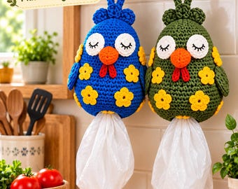 May include: Two crochet chicken plastic bag holders hanging from a black rack. One is blue and one is olive green. Both feature white eyes with black lashes, orange beaks, red wattles, and yellow flower appliqués. White plastic bags hang below.