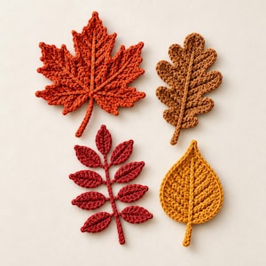 Puede incluir: Un conjunto de cuatro aplicaciones de hojas tejidas a ganchillo en colores otoñales. La colección incluye una hoja de arce naranja grande, una hoja de roble marrón, una hoja compuesta de color rojo oscuro con varios folíolos y una hoja ovalada amarilla.