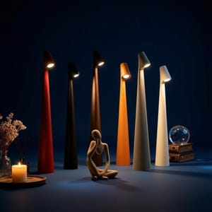 May include: Six tall, slender, conical floor lamps in red, black, dark brown, orange, light gray, and white, each with a small, angled light source at the top. A small abstract human figure sculpture sits in front of the lamps on a dark surface.