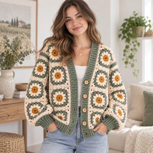 May include: A crochet cardigan featuring a repeating daisy granny square pattern in cream, sage green, and mustard yellow. The garment has a V-neckline, long sleeves with ribbed cuffs, and a sage green button-down front with four wooden buttons.