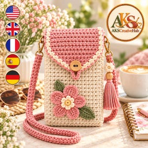 Op de afbeelding: Een gehaakte crossbody telefoontas van crème en oudroze garen. De tas heeft een roze flap met een houten knoopsluiting, een roze gevlochten schouderband en een grote roze bloemapplicatie met groene bladeren aan de voorzijde.
