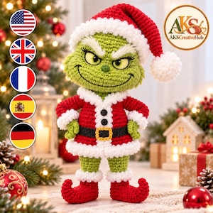 Puede incluir: Un muñeco de ganchillo verde con un traje de Papá Noel rojo con ribetes blancos esponjosos, un gorro rojo a juego con un pompón blanco y zapatos rojos de punta curvada. La figura tiene una expresión gruñona, ojos amarillos y un cinturón negro.