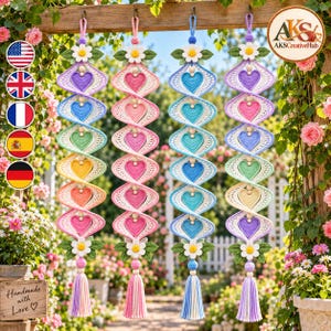 May include: Four vertical hanging decorations featuring a spiral design with crocheted hearts in various pastel colors. Each piece is topped and bottomed with a white daisy and green leaves, ending in a long, multi-colored yarn tassel.