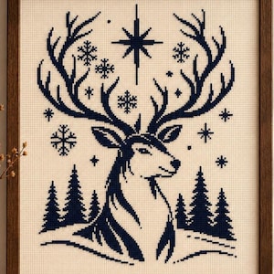 Peut inclure: Une broderie au point de croix encadrée représentant la silhouette d'un cerf bleu foncé sur un fond en tissu crème. Le motif comprend une grande étoile, divers flocons de neige et une rangée de sapins à la base du cerf.