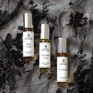 May include: Three small glass bottles of perfume with silver caps and labels. The labels are white with black text and feature the brand name "Immortal Perfumes" and the names of the scents: "Baby Vamp", "Untamed Lady", and "Fairbanks". All three bottles are part of the "Old Hollywood" series.
