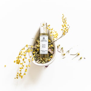 May include: A small glass bottle of perfume with a white label that reads "Jane Eyre" and "Library Lotion Series". The bottle is sitting in a white ceramic bowl filled with dried flowers and yellow flower sprigs.