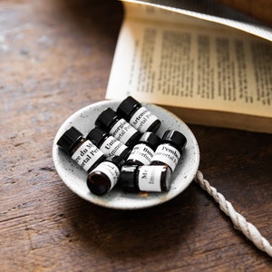 May include: A small white ceramic dish with eight small glass bottles containing essential oils. The bottles are labeled with the names of the scents, including "Tre du My", "Georgian", "Untaortal", "Artemis", "Pember", "Mr", "Imm", and "Bun".
