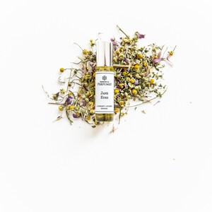 May include: A small glass bottle of perfume with a white label that reads "Elemental Perfumes Jane Eyre Literary Lovers Series". The bottle is surrounded by dried chamomile flowers.