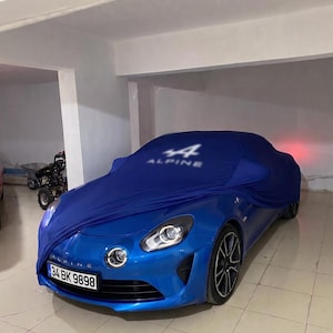 May include: A bright blue Alpine sports car with a number plate reading 34 BK 9898. The front half of the vehicle is exposed, while the rear is covered by a dark blue fabric car cover featuring the white Alpine logo and the number 44.