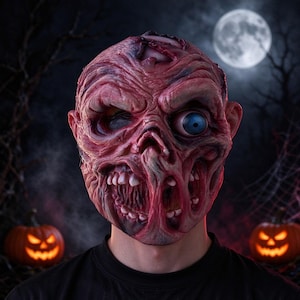 Könnte beinhalten: Eine Vollkopf-Latexmaske, die ein groteskes, fleischiges und strukturiertes Zombigesicht mit entblößten Zähnen, tiefen Falten und einem großen, hervorstehenden blauen Auge zeigt. Die Maske hat einen rohen, rötlich-rosa Hautton mit Schattierungen.