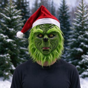 Puede incluir: Una máscara de personaje verde y texturizada con ojos amarillos, una nariz pequeña negra y el ceño fruncido, con pelo sintético largo verde alrededor de la barbilla y las mejillas. La máscara lleva un gorro de Papá Noel rojo y blanco.