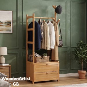 May include: A light-coloured wooden garment rack featuring a top hanging rod, side hooks, and two bottom drawers. The rack holds a dark blue blazer, a patterned scarf, a beige knit sweater, a white shirt, a tan coat, and a dark beanie.