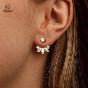 May include: A gold ear jacket earring featuring a single round brilliant-cut stone stud at the top and a curved, fan-shaped attachment below. The attachment is adorned with five marquise-cut stones and two round stones, creating a layered effect.