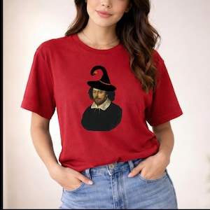 Peut inclure: Un t-shirt rouge à manches courtes avec une impression graphique de William Shakespeare portant un chapeau de sorcière noir pointu avec un accent orange. Le t-shirt a un col rond et est associé à un jean bleu, créant un look décontracté.