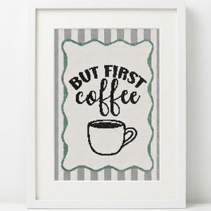 May include: A framed cross-stitch wall art piece featuring a white background with a gray striped border. The center displays the black text "BUT FIRST coffee" above a black outlined coffee cup. The design is enclosed in a scalloped green frame.