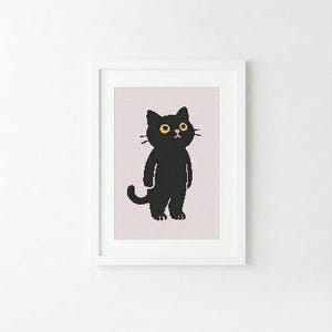 May include: A framed cross-stitch embroidery featuring a pixelated black cat with large yellow eyes and a small pink nose, standing upright on a light pink background, enclosed within a simple white rectangular frame.