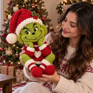 Könnte beinhalten: Eine gehäkelte grüne Kreaturenpuppe mit schelmischem Gesichtsausdruck, die eine rot-weiße Weihnachtsmütze mit Bommel, einen roten Pullover mit weißem Herz sowie passende rot-weiß gestreifte Beinwärmer mit roten Füßen trägt.