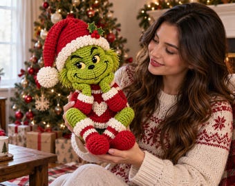 May include: A crocheted green creature doll with a mischievous expression, wearing a red and white Santa hat with a pom-pom, a red sweater featuring a white heart, and matching red and white striped leg warmers with red feet.