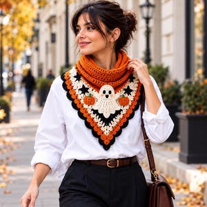 May include: A crochet cowl featuring a Halloween theme with a central white ghost, two orange pumpkins, and black star motifs. The triangular-shaped accessory is crafted with orange, white, and black yarn, worn over a white button-down shirt.