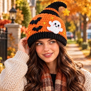 May include: A crocheted beanie hat featuring a black brim and an orange crown. The hat is decorated with two black bats, a white ghost with pink cheeks, and a yellow star dangling from the pointed top. The design includes small yellow cross-stitch accents.