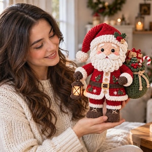 Puede incluir: Un muñeco de Papá Noel tejido a ganchillo con un traje rojo y blanco y un gorro a juego, que sostiene una pequeña linterna iluminada en una mano y un saco verde lleno de regalos y un bastón de caramelo en la otra, con costuras y botones.