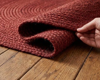 Könnte beinhalten: Ein tiefroter geflochtener Teppich mit einer dicken, strukturierten Webart. Der Teppich besteht aus konzentrischen kreisförmigen Reihen fest gedrehter Fasern, die ein haltbares und gleichmäßiges Oberflächenmuster bilden, das beim Anheben sichtbar wird.
