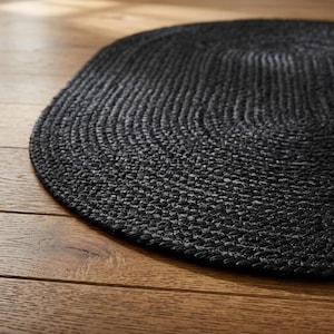 Könnte beinhalten: Ein ovaler Teppich mit einer dichten, geflochtenen Textur in einheitlichem Schwarz. Der Teppich besteht aus miteinander verwobenen Strängen, die ein konsistentes, sich wiederholendes Muster über die gesamte Oberfläche des Bodenbelags bilden.