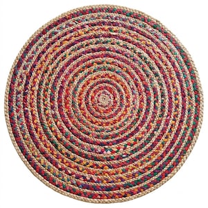 May include: A round braided rug featuring concentric circles of natural tan jute fibers interspersed with vibrant, multi-colored fabric strips in shades of red, yellow, green, and purple, creating a textured, circular pattern throughout the piece.