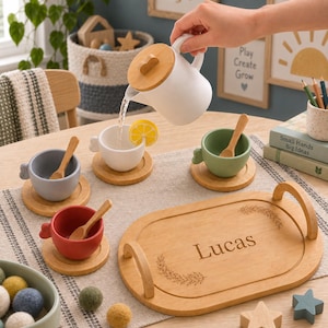 Op de afbeelding: Een houten theeservies met een witte theepot met houten deksel, vier kleurrijke keramische kopjes in wit, grijs, groen en rood, elk met een houten lepel en onderzetter. Een ovaal houten dienblad is gegraveerd met de naam Lucas en bladmotieven.