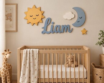 Könnte beinhalten: Ein Wanddekorationsset aus Holz mit einer gelben Sonne mit schlafendem Gesicht, einem blauen Halbmond mit schlafendem Gesicht, einer weißen Wolke, einem kleinen gelben Stern und dem Namen Liam in blauer Schreibschrift über einem Holzbettchen.